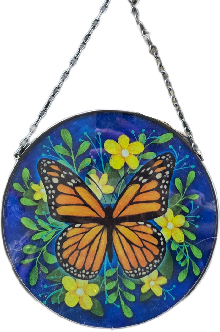 A circular hanging glass art piece featuring a painted monarch butterfly, green leaves, and yellow flowers on a deep blue background, suspended by a black metal chain.